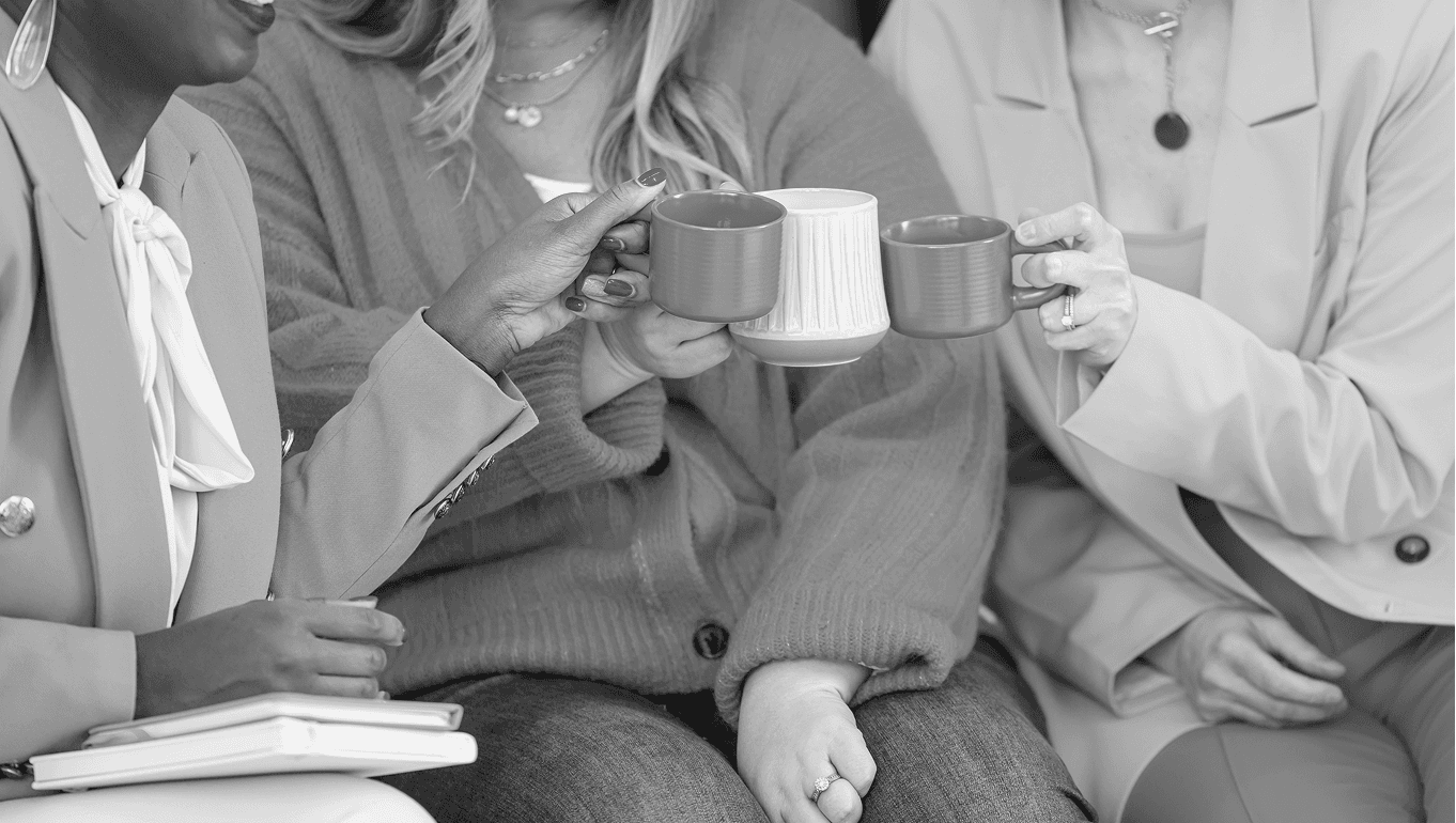A grayscale image of seated women with coffee mugs.