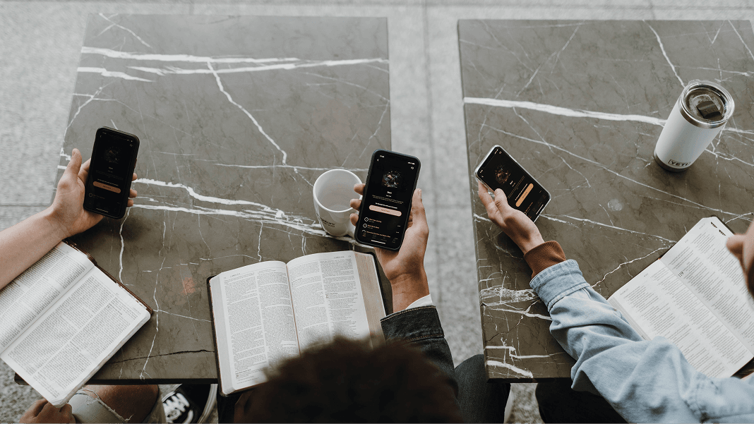 Three individuals seated at a table with Bibles and smartphones.