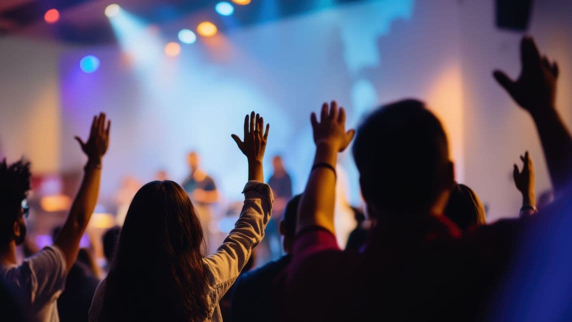 People with raised hands in a worship setting, representing engagement and unity.