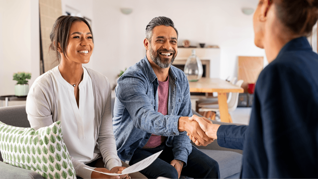 Smiling couple shaking hands with advisor in a professional setting, representing financial advisory services.