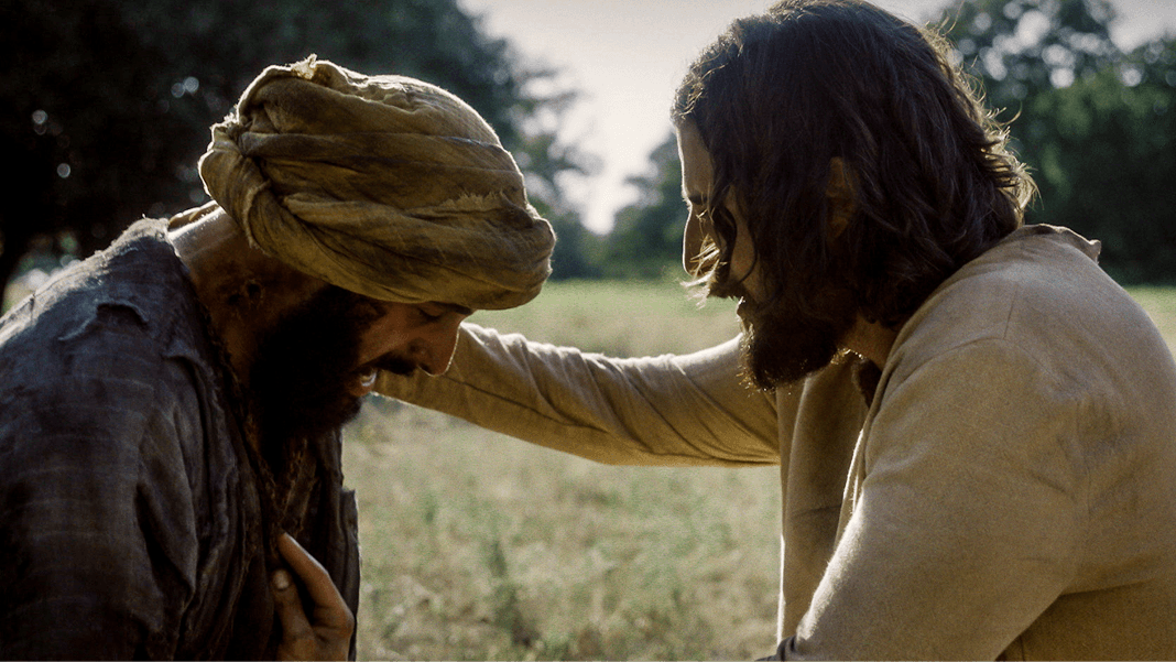 Jesus comforts a distressed man wearing a headwrap in an open field.
