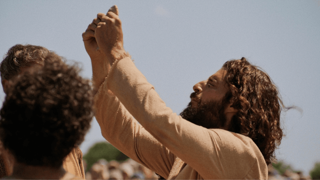 Jesus looks upward with raised arms in daylight.