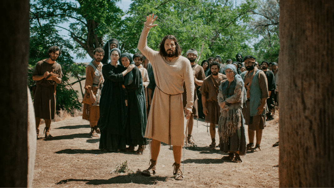 Jesus stands with arm raised before a group of concerned onlookers.