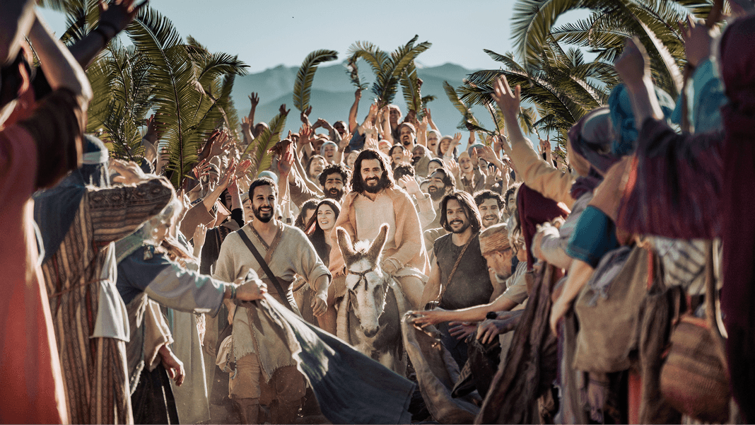 Jesus rides a donkey through a cheering crowd waving palm branches.